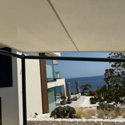 Θέα κάτω από το σκίαστρο με τμήμα μοντέρνου κτιρίου και θαλάσσιο τοπίο στη Νέα Πέραμο